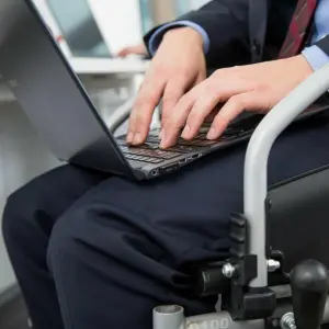 Ein Mann im Rollstuhl arbeitet an Laptop im Büro