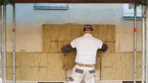 Ein Handwerker dämmt die Fassade eines Hauses
