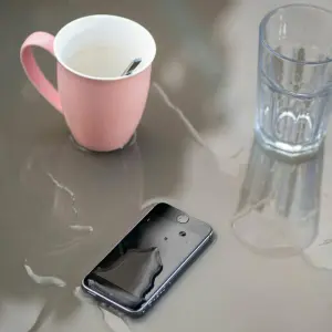 Ein nasses Smartphone neben Tasse und Glas