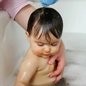 Ein Kleinkind sitzt, gehalten von einer Hand, in der Badewanne.