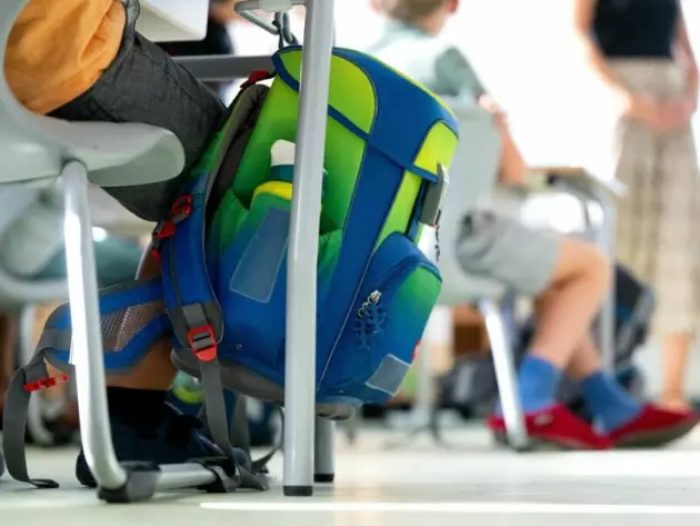 Ein Rucksack hängt im Klassenzimmer am Tisch eines Grundschülers