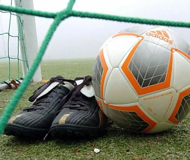 Fußballschuhe und ein Ball liegen hinter einem Tornetz