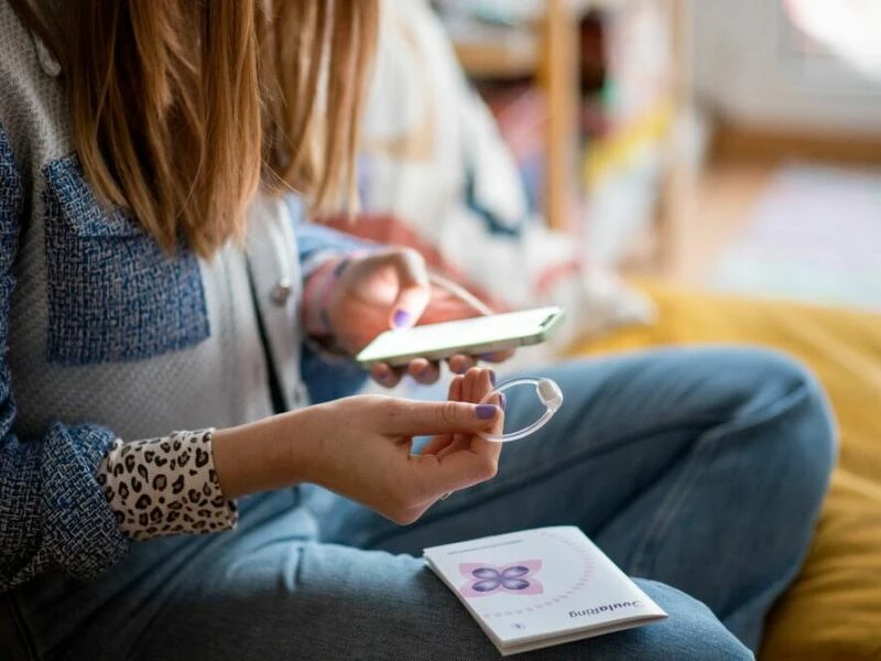 Eine Frau hält den Ovularing und ihr Smartphone in den Händen