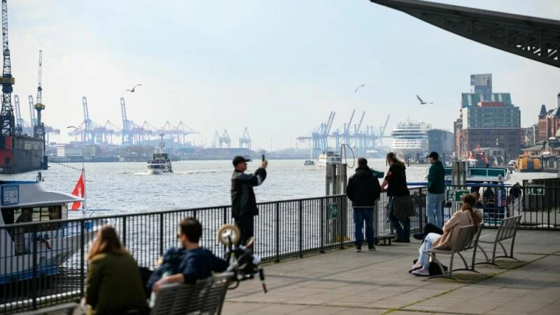 Passanten auf den Landungsbrücken vor der Hafenkulisse