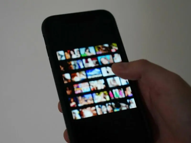 Ein Mann scrollt auf seinem Handy durch eine Pornoseite