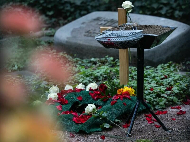 Frisches Urnengrab mit Holzkreuz und Blumen