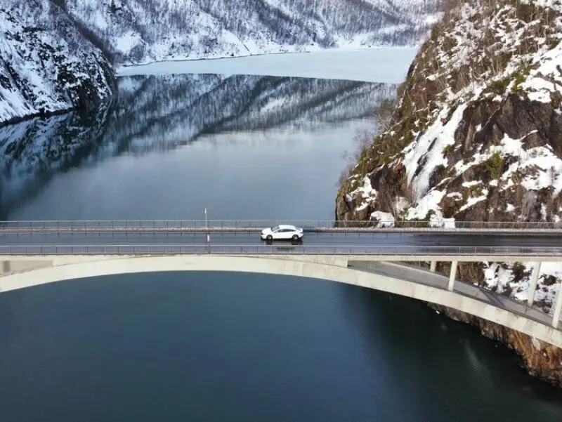 Ein E-Auto fährt über eine Brücke, die über einen Fjord führt
