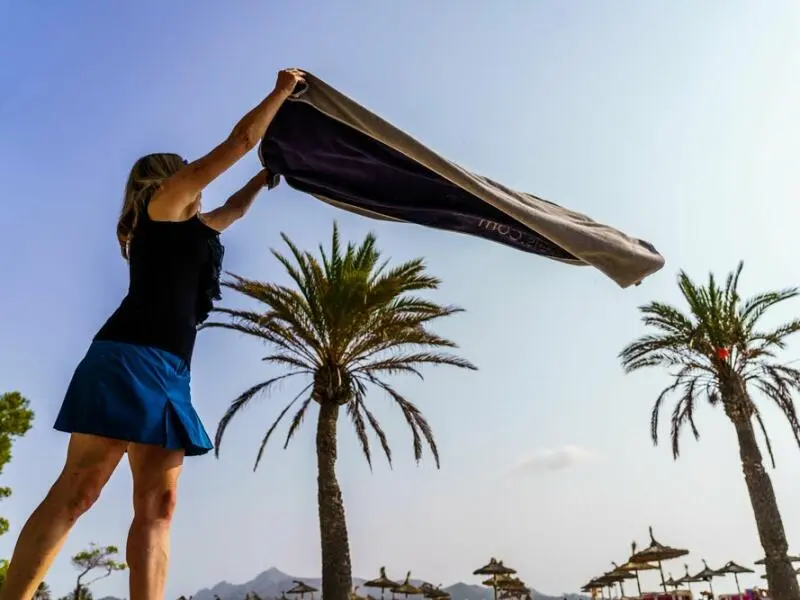 Eine Frau breitet am Strand ihr Handtuch aus