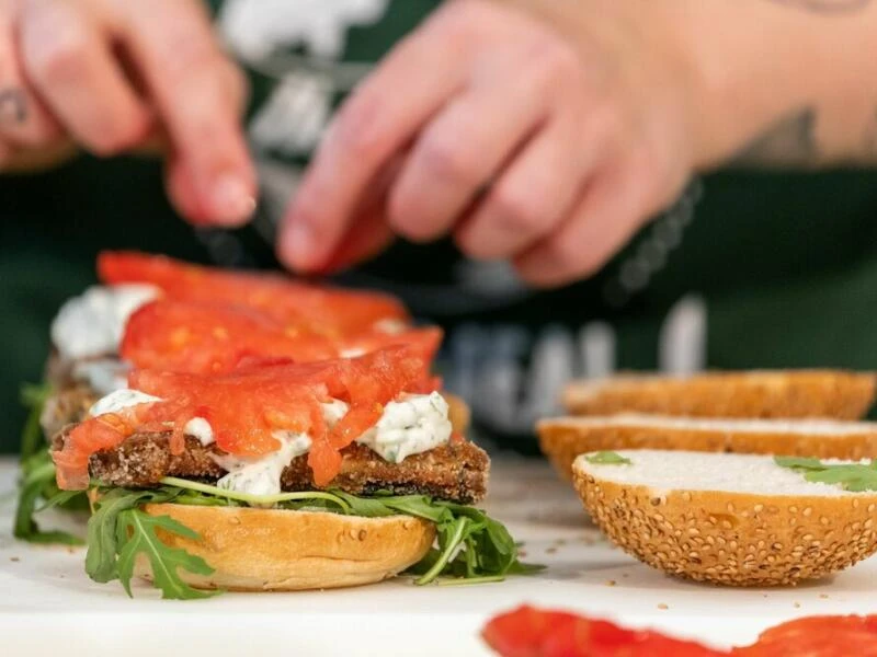 Eine Köchin belegt einen Burger mit veganem Fischersatz