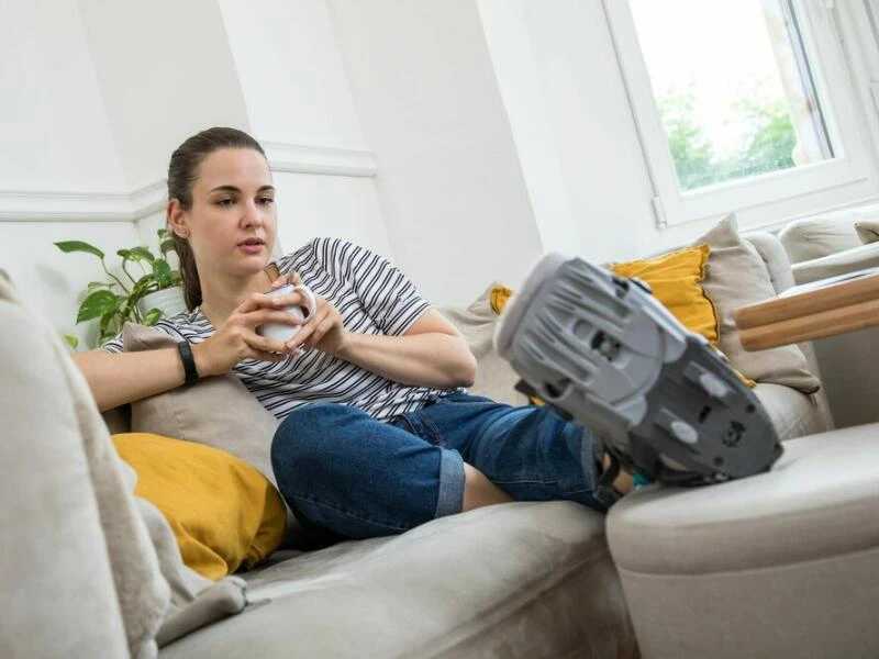 Eine Frau liegt mit einer Orthese auf dem Sofa