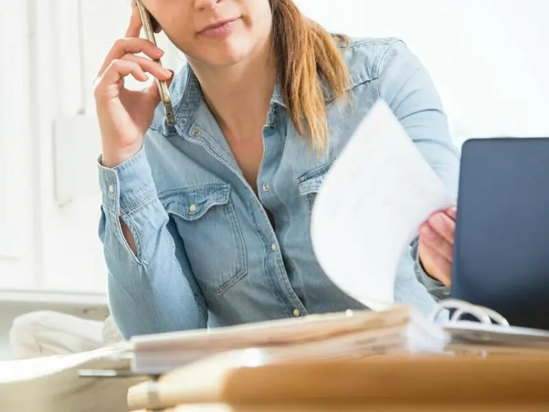 Eine Frau telefoniert und liest Unterlagen durch