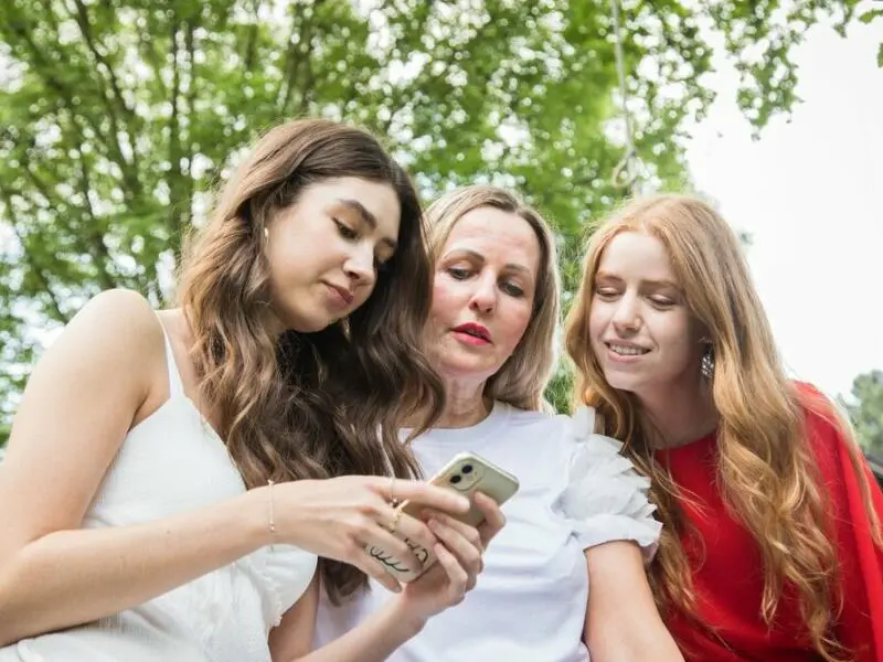 Ein Frau schaut mit zwei Mädchen auf ein Smartphone.