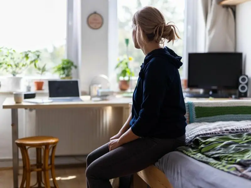 Eine Studentin sitzt auf dem Bett in ihrem WG-Zimmer