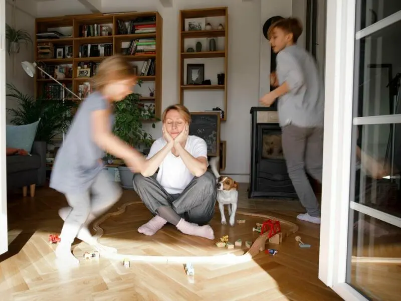 Gestresste Mutter sitzt zwischen dem Spielzeug ihrer Kinder