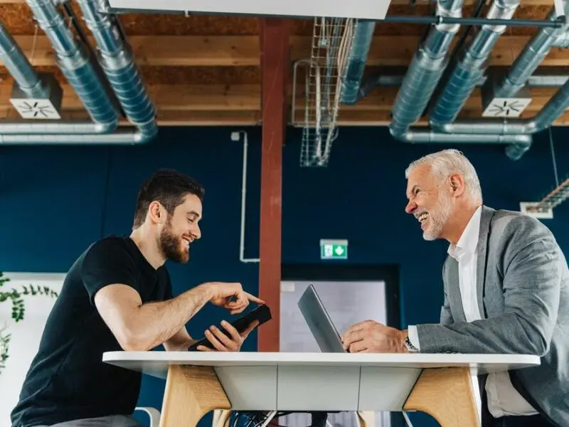 Jüngerer und älterer Mensch sprechen in modernem Büro miteinander