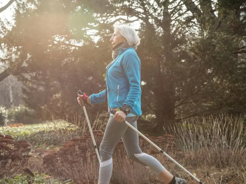 Eine ältere Frau ist mit Nordic-Walking-Stöcken unterwegs