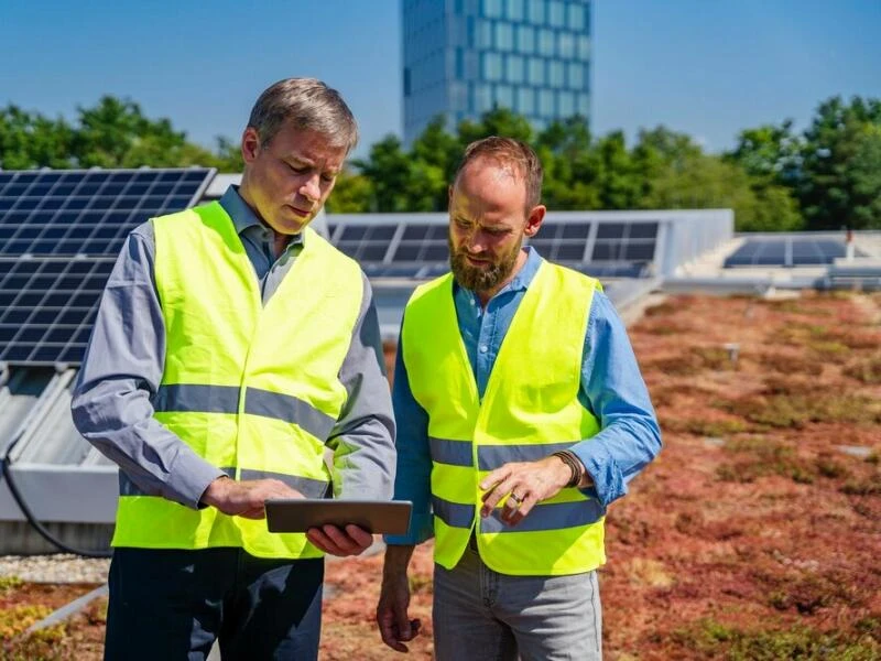 Zwei Arbeiter stehen auf dem begrünten Dach vor einer Solaranlage