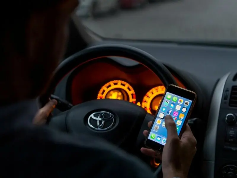 Ein Mann sitzt mit Handy in der Hand in einem Auto am Steuer