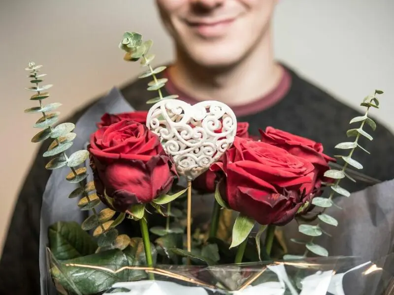 Ein grinsender Mann hält Rosen in der Hand