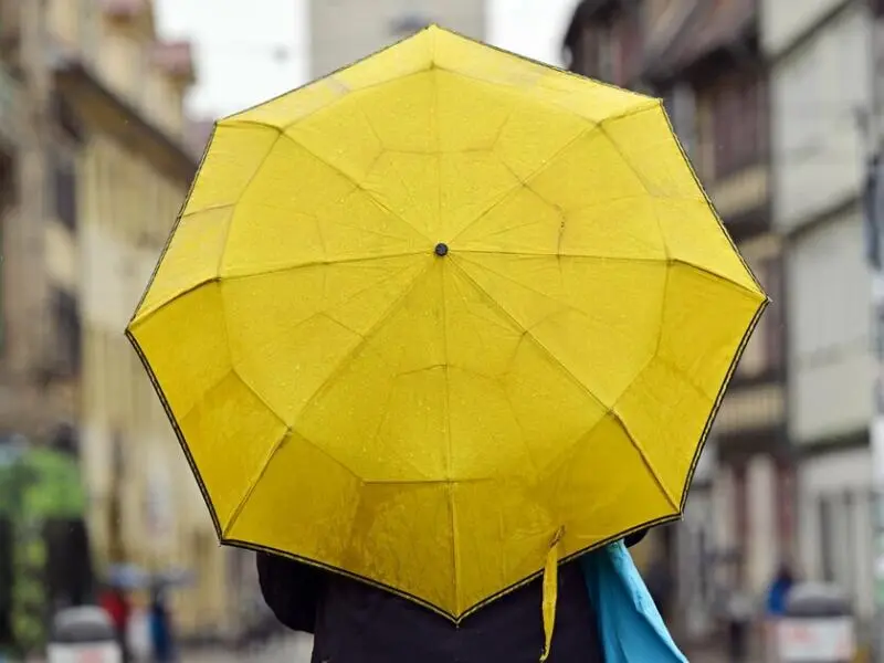 Eine Passantin mit gelbem Regenschirm