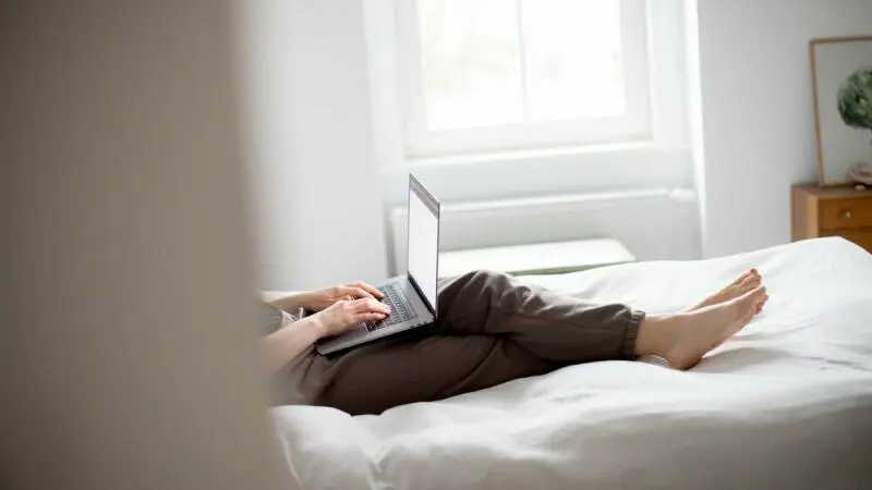 Eine Frau sitzt mit Laptop im Bett