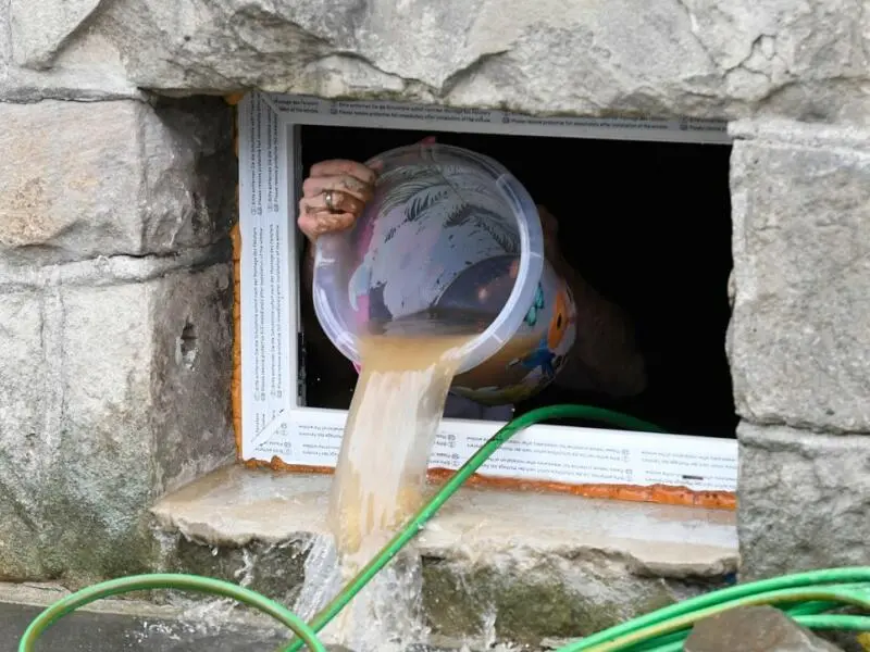 Eine Person schippt mit einem Eimer Wasser aus einem Fenster