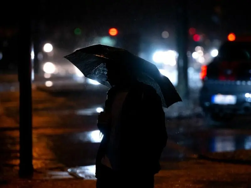 Ein Fußgänger geht in München bei Regen über eine Kreuzung