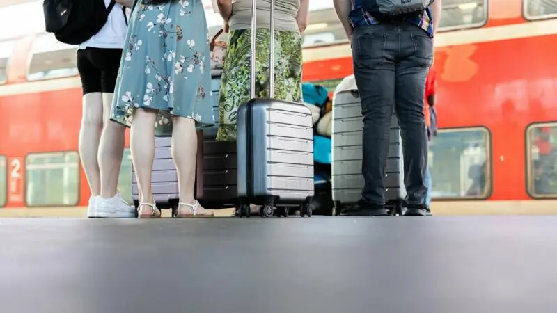 Personen stehen mit Koffern auf einem Bahnsteig