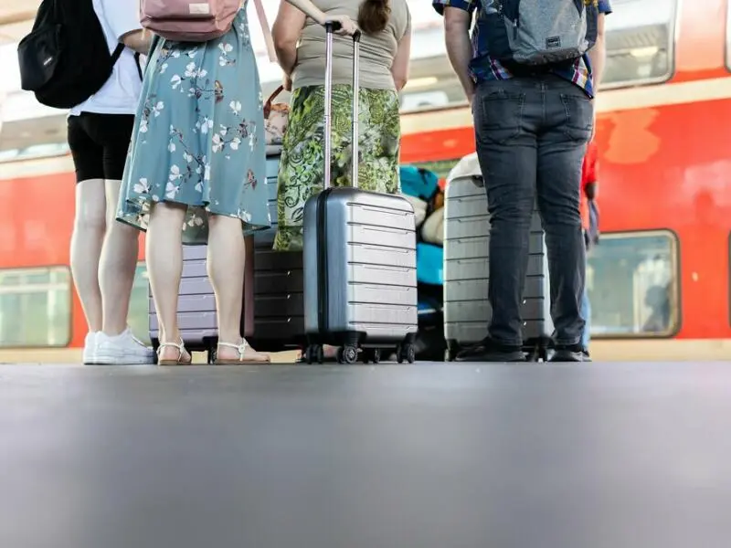 Personen stehen mit Koffern auf einem Bahnsteig