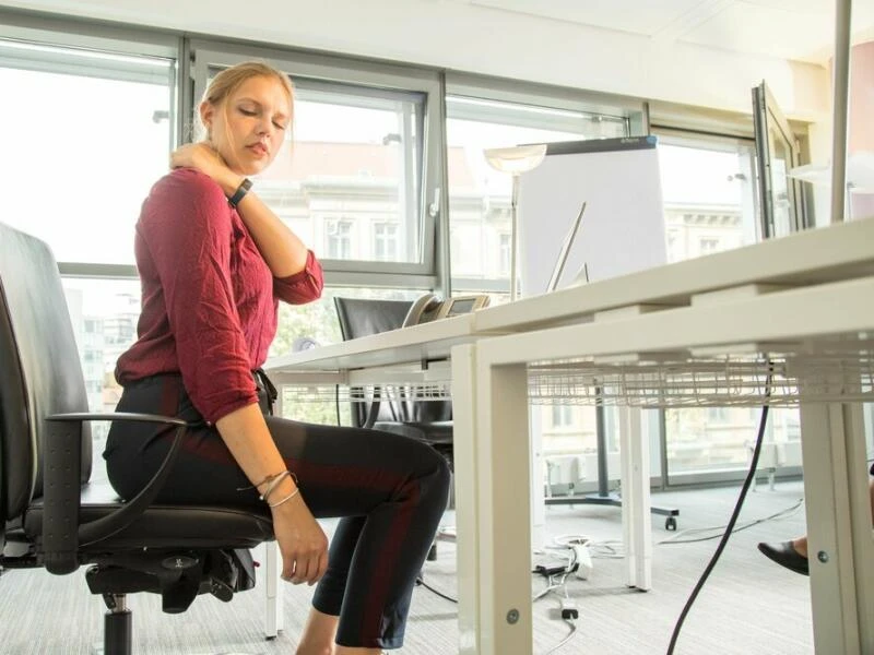 Eine Frau sitzt in einem Büro und hat Nackenschmerzen