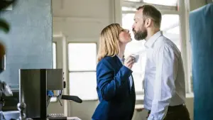 Zwei Personen küssen sich in einem Büro
