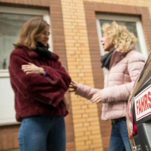 Zwei Frauen im Gespräch hinter Fahrschulwagen