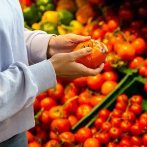 Eine Frau begutachtet eine Tomate in einem Supermarkt