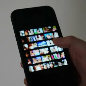 Ein Mann scrollt auf seinem Handy durch eine Pornoseite