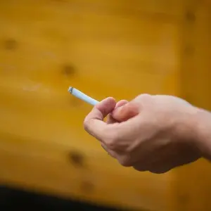 Ein Mann hält eine brennende Zigarette in der Hand