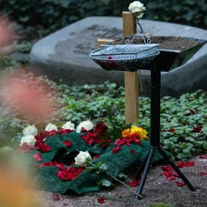 Frisches Urnengrab mit Holzkreuz und Blumen