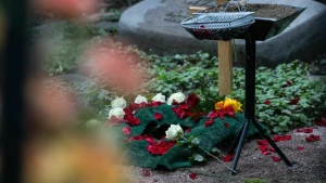 Frisches Urnengrab mit Holzkreuz und Blumen