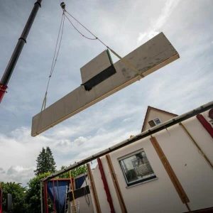 Ein Kran hebt eine vorgefertigte Wand auf einer Baustelle