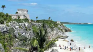 Eine Maya-Ruine und Palmen auf über dem Strand und türkisem Meer.
