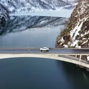 Ein E-Auto fährt über eine Brücke, die über einen Fjord führt