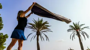 Eine Frau breitet am Strand ihr Handtuch aus