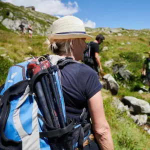 Eine Frau wandert mit Rucksack und Hut an einem Berg