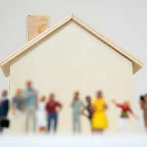 Viele Menschenfiguren vor einem Hausmodell