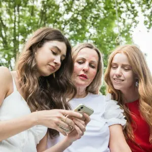 Ein Frau schaut mit zwei Mädchen auf ein Smartphone.