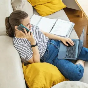 Eine Frau mit Telefon und Laptop auf einem Sofa