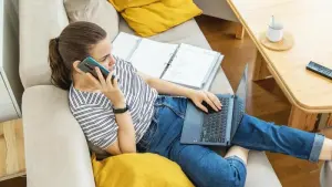 Eine Frau mit Telefon und Laptop auf einem Sofa