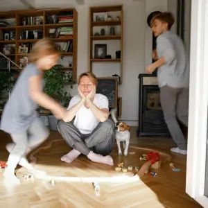 Gestresste Mutter sitzt zwischen dem Spielzeug ihrer Kinder