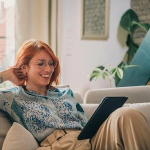 Eine Frau sitzt auf einer Couch und bedient ein Tablet