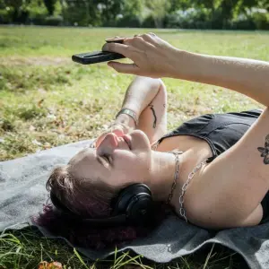 Eine Frau liegt auf der Wiese und hört etwas über ihr Handy