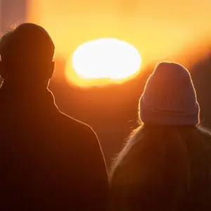 Ein Paar blickt nebeneinander in einen Sonnenuntergang